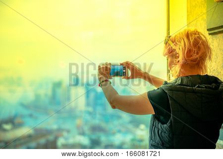 Scenic view of Hong Kong skyline at sunset. Observation deck with defocused background. Young tourist taking picture with smartphone enjoying view over Victoria Harbour.Travel and tourism asia concept
