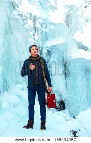Handsome guy smiling in the snowy forest and frozen waterfall