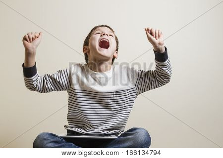 Winning a game. Happy boy screeming euphoric sitting with digital tablet computer. Technology, gaming concept