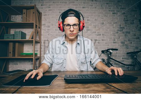 Young man playing game at home and streaming playthrough or walkthrough video. Attractive guy in cab and earphones looking at the camera. He seems to be shocked because of vr