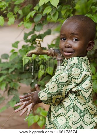 Young African school boy holding hands under a tap. Water scarcity problems concern the inadequate access to safe drinking water. 1 billion people in the developing world don't have access to it.