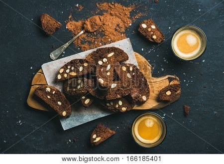 Dark chocolate and sea salt Biscotti with almonds and two glasses of coffee espresso on wooden serving board over dark stone background, top view