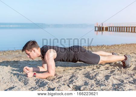 Fit man doing pank exercise during training workout on beach in summer