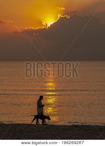 man walking with a dog on a beach with sunset