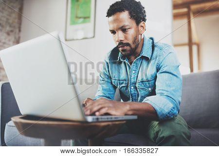 Concentrated bearded African man working at home while sitting on the sofa.Concept of young people using mobile devices.Blurred background