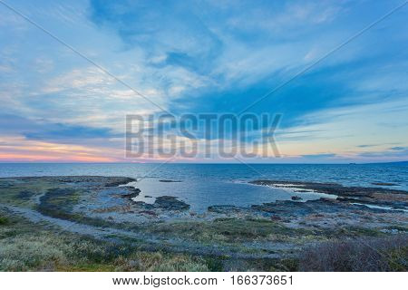 View over the seafront of the city Paphos in Cyrpus. Palm silhouettes, boats in the water and golden sunset over the sea with dramatic cloudy sky.
