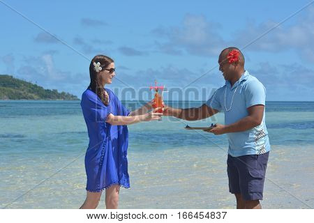 Fijian man serve a tropical cocktail drink to a tourist woman in a resort on an island in Fiji. Travel holiday vacation concept. Real people copy space