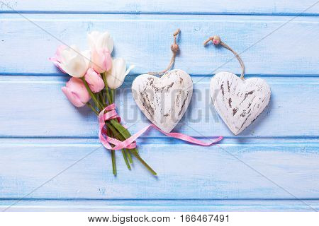 White and pink spring tulips and two decorative hearts on blue background. Pastel colors. Shubby chic. Selective focus.