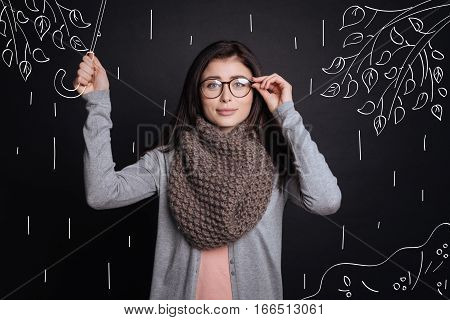 Enjoy the weather. Pleasant nice young beautiufl woman touching her glasses and holding umbrella while walking
