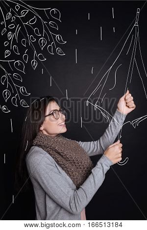 Good protection. Delighted smiling young woman opening her umbrella and enjoying the rain while expressing gladness