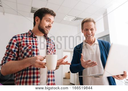 What do you think about this. Handsome cheerful pleasant man holding a laptop and showing something on it to his colleague while asking his opinion