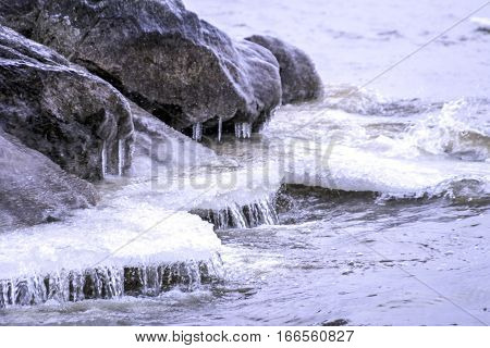 Water and ice on shoreline covering rocks and forming icicles winter closeup scene