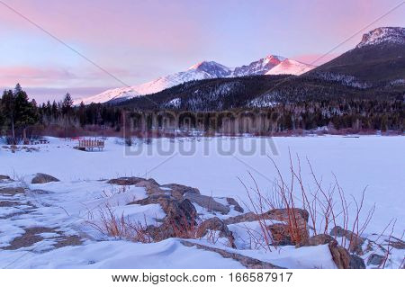The summit of Longs Peak glows with a snow covered Lily Lake in the foreground