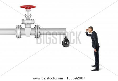 Businessman on white background looking at pipe with a red valve that's leaking one big drop of oil. Oil and gas industry. Commodities trade. Business and success.