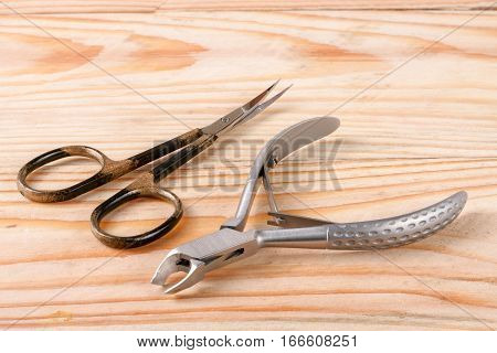 nail scissors and clippers to remove the cuticle and nail care products on a light wooden background.
