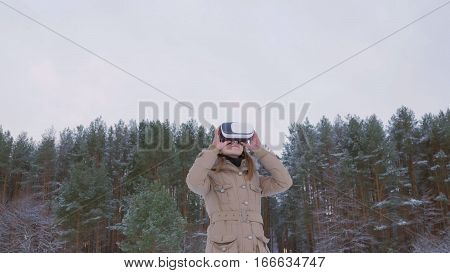 Woman putting on and using virtual reality glasses in winter forest. Virtual reality mask. VR. Future, nature, winter and technology concept