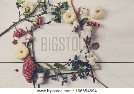 Floral composition. Frame made of dried fall flowers, pumpkins, branches and autumn leaves, also cotton, clove and sloe. Top view on white wood, flat lay, copy space on paper sheet.