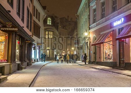 TALLINN ESTONIA - 4TH JAN 2017: A view along Pikk street in Tallinn Old Town at night during the winter. Snow people restaurants and shops can be seen.