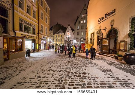 TALLINN ESTONIA - 4TH JAN 2017: A view along streets of Tallinn Old Town at night during the winter. Snow people restaurants and shops can be seen.