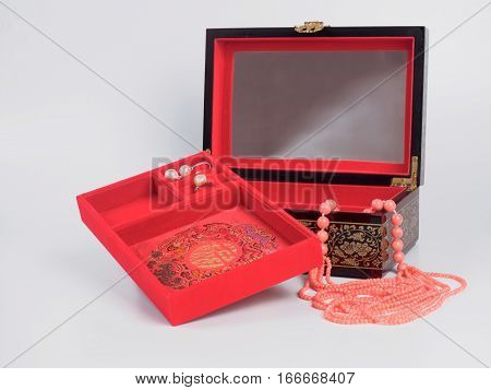 Picture of the opened jewel-box with red fit-out. Wooden jewel-box with pink coral bead necklace on white background. Side view.
