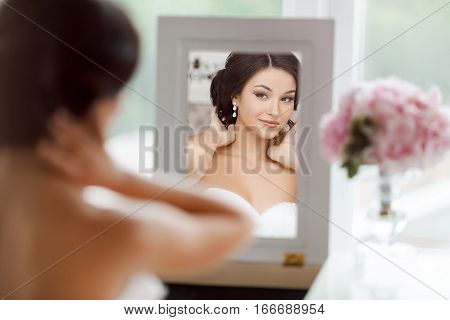 Portrait of young beautiful bride preparing to her wedding day. Gorgeous woman looking at mirror at her make-up and hairstyle
