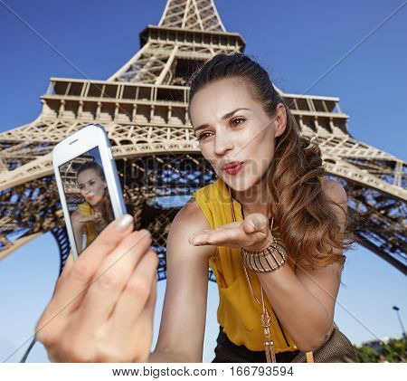 Woman Taking Selfie And Blowing Air Kiss Near Eiffel Tower