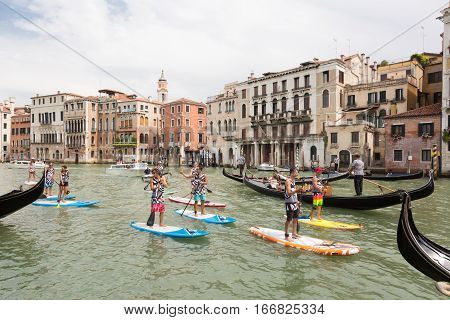 Venice, Italy - July 24, 2016: Group of sporty active tourists stand up paddling on sup boards in guided organized group on historical Grand Canal on 24th of July in Venice, Italy.