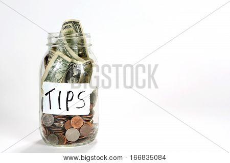Glass canning jar with coins and dollar bills of money have a label with tips written on it.