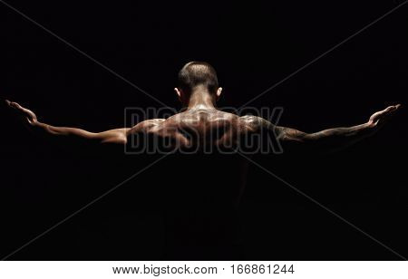 Unrecognizable man bodybuilder shows strong hands and neck muscles, athletic trapezius. Low key, studio shot on black background.
