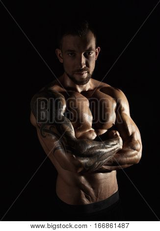 Strong athletic man. Handsome male fitness model showing naked torso, muscular body. Strong hands, chest and shoulder muscles and biceps. Studio shot on black background, low key. Bodybuilding concept