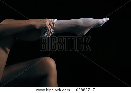 Low key photo of sexy woman put on her white nylon stockings on long fit legs against dark background horizontal view