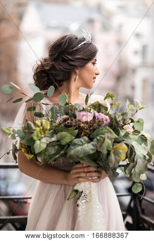 bride with a bouquet of flowers on the balcony among the streets of the big city