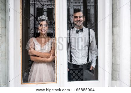 The bride and groom standing near a large window. The couple smile and dream.