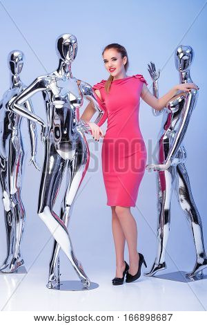 beautiful smile woman in pink evening dress on  background of many fashion shiny metallic mannequins. the uniqueness.