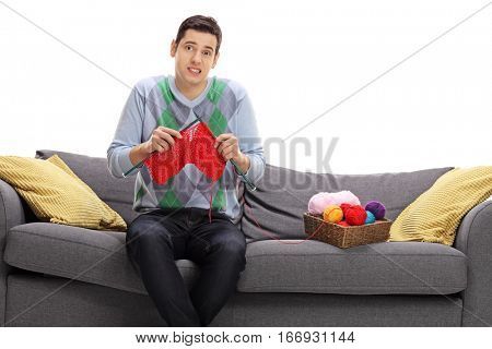 Confused young man attempting to knit and looking at the camera isolated on white background