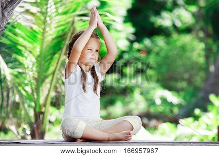 Child doing exercise on wooden platform outdoors. Healthy lifestyle. Yoga girl