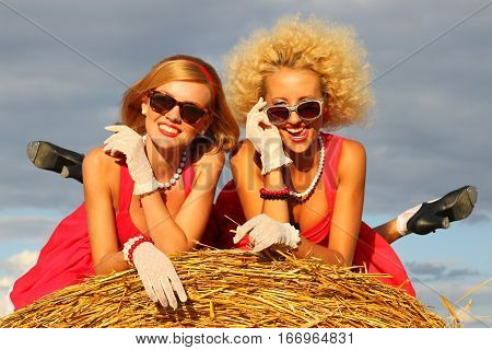 Two smiling retro girls liying oh the hay.