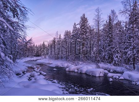 Stunning Winter Lapland Landscape With Beautiful Sunset, Non-frozen River And Snow-covered Forest. U