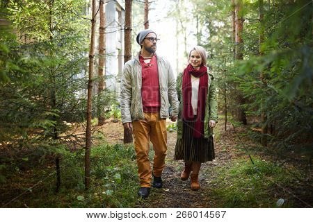 Young stylish Caucasian couple holding hands while walking in forest on ...