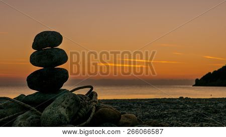 Beach Stone Fireplace With Rope At Sunrise. Sea Water With Rocks In The Background. Vlychada Beach P