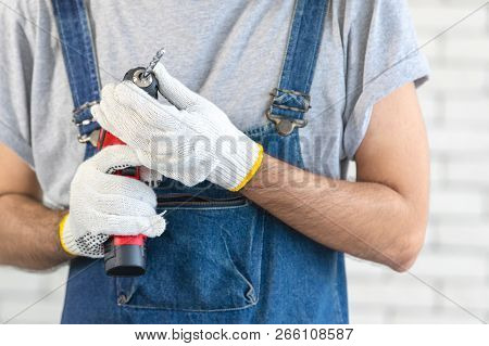 Young Asian Man Holding Power Drill Standing In Front Of White Brick Wall, Smiling And Looking At Ca