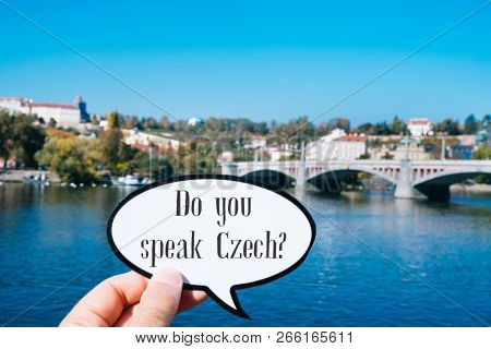 closeup of the hand of a young caucasian man showing a speech bubble with the question do you speak Czech written in it, next to the Vltava river in Prague, Czech Republic