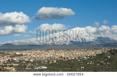 Bronte town under the snowy and majestic volcano Etna and a cloudy blue sky