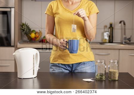 Woman Making A Cup Of Tea In The Morning, Holding  A Cup And Adding A Teabag Into A Boiling Water Fr