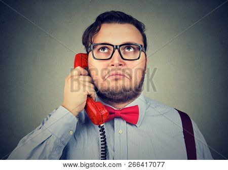 Adult Chunky Man In Red Bow Tie And Glasses Speaking On Telephone Looking Up In Puzzlement