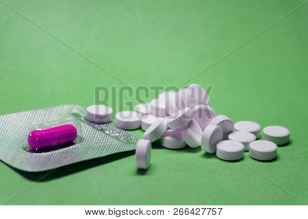 Purple (magneta), Pink Capsule Pills In A Blister And White Round Pills In Bulk On A Green Backgroun