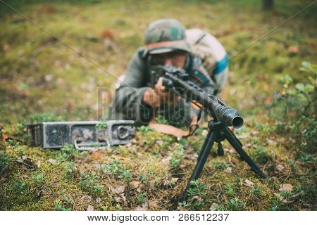 Hidden Unidentified Re-enactor Dressed As German Wehrmacht Soldier Aiming A Machine Gun At Enemy Fro