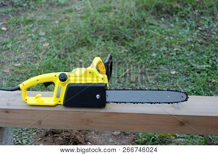 New Black And Yellow Electric Saw On Brown Wooden Balk Ready For Work Outdoors Closeup View