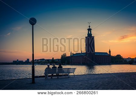 Silhouette Of Women Sitting On Bench At Promenade Quay Bank Of Lake Malaren Looking At Stockholm Cit