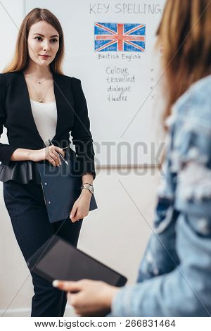 Two Female Students Talking In Classroom. College, English Language School.